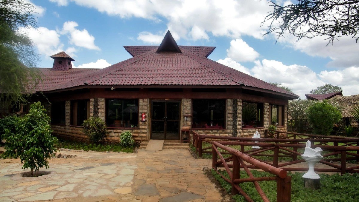 Thatched stone lodge building with manicured gardens beneath a wide sky at AA Lodge Amboseli.
