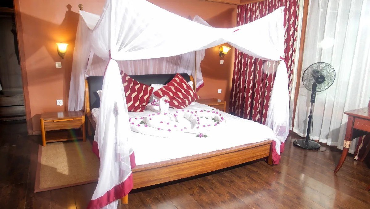 Four-poster bed under white mosquito netting with red trim at AA Lodge Amboseli.