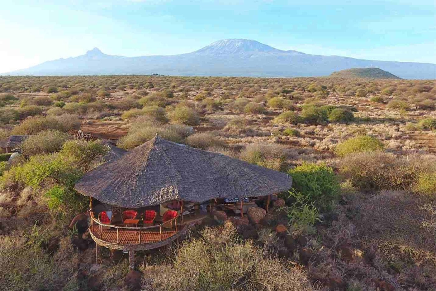 Thatched camp buildings overlooking the savanna with Mount Kilimanjaro behind at Amboseli Bush Camp.