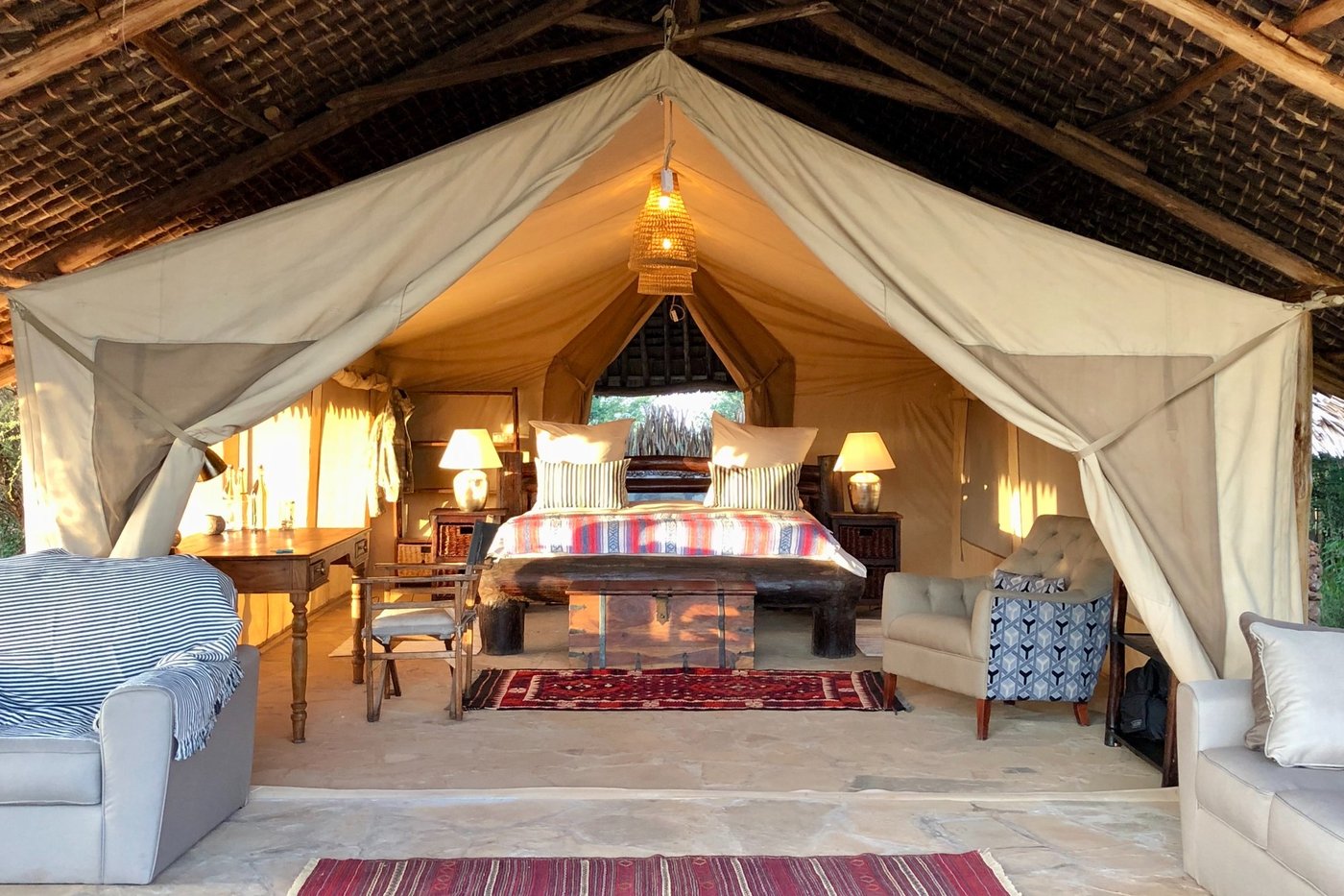 Safari tent bedroom with patterned bedspread and open canvas sides at Amboseli Bush Camp.