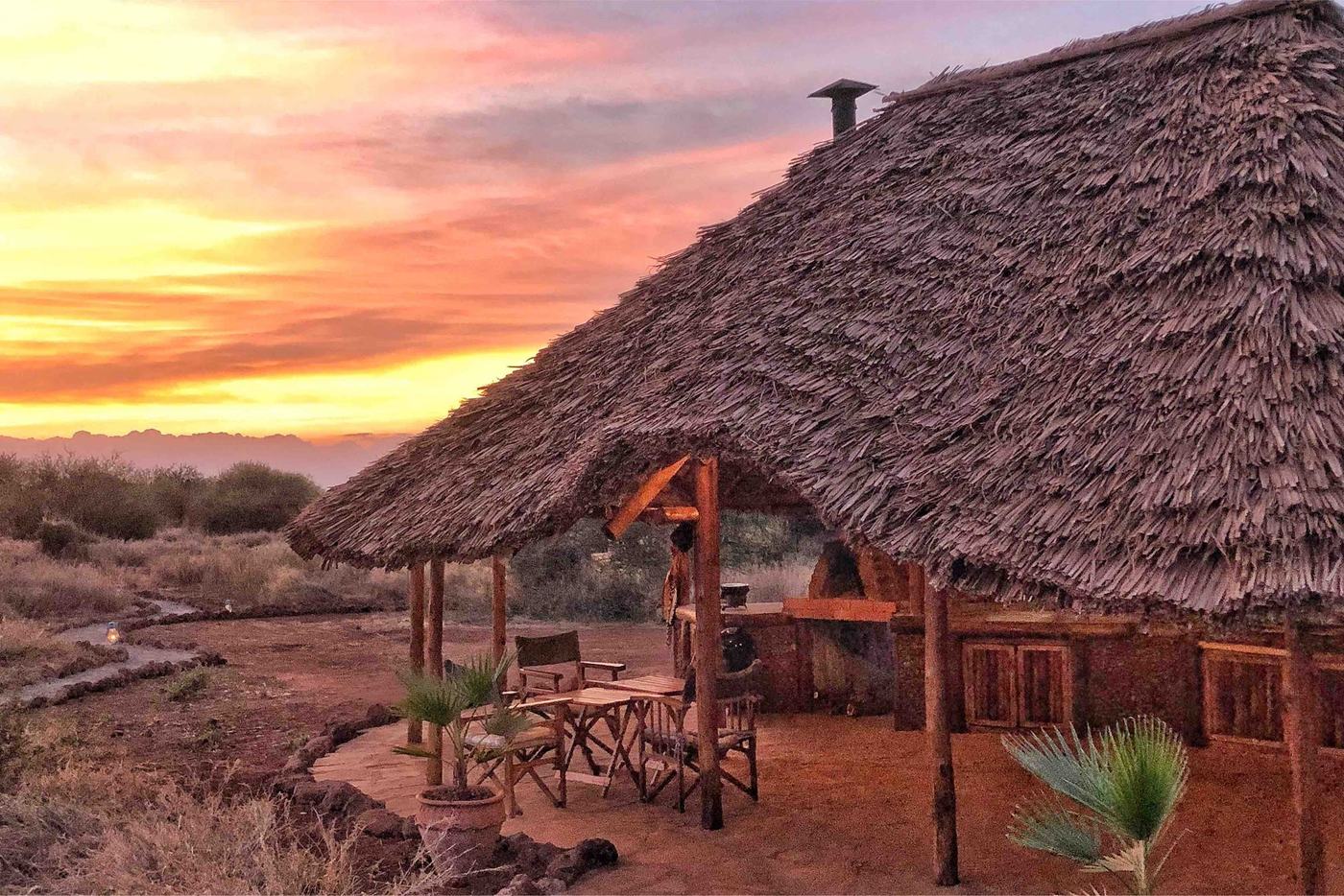 Thatched mess tent silhouetted against an orange sunset sky at Amboseli Bush Camp.