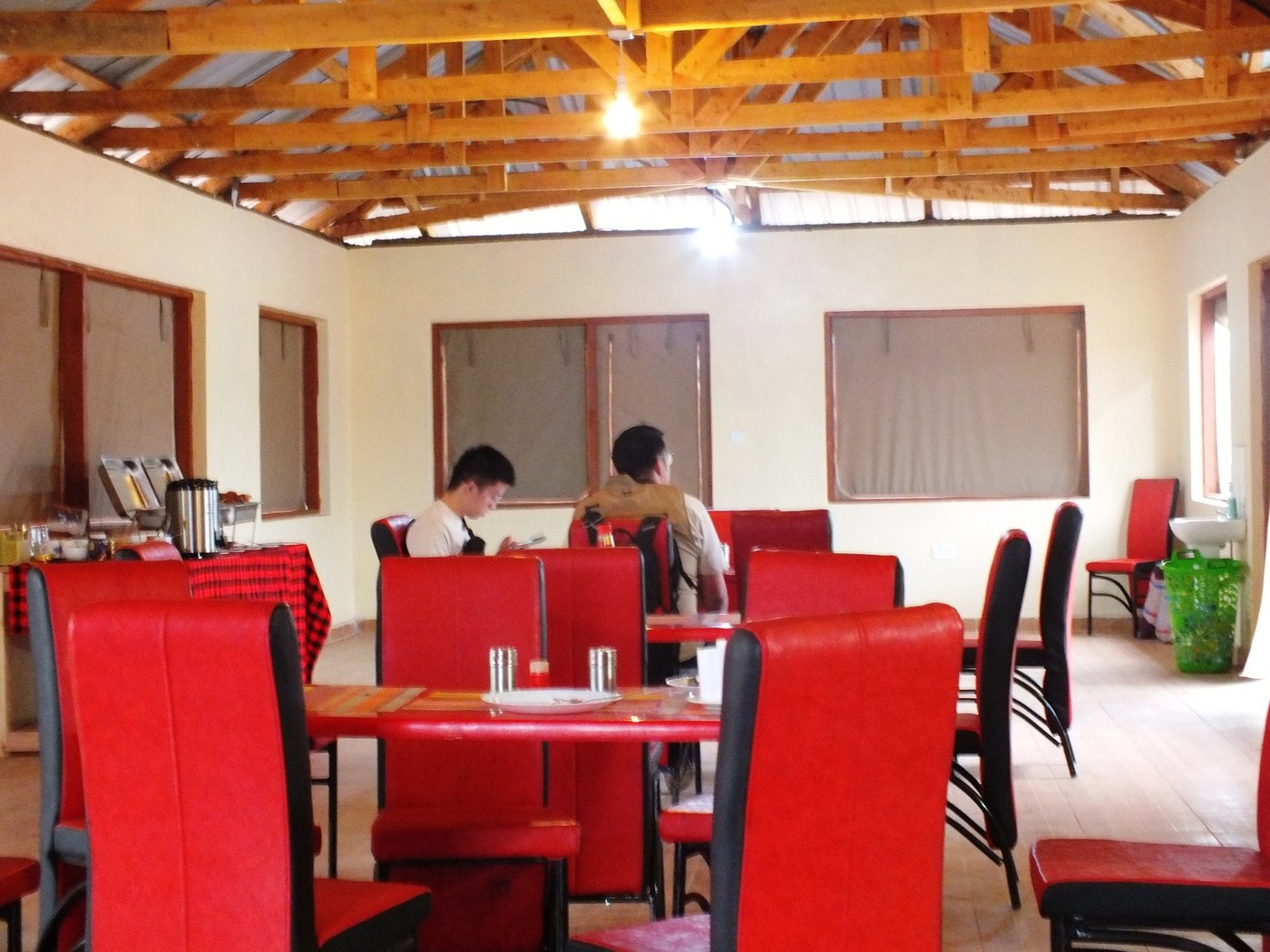 Red dining chairs and tables set in the mess tent at Amboseli Mountain View Camp.
