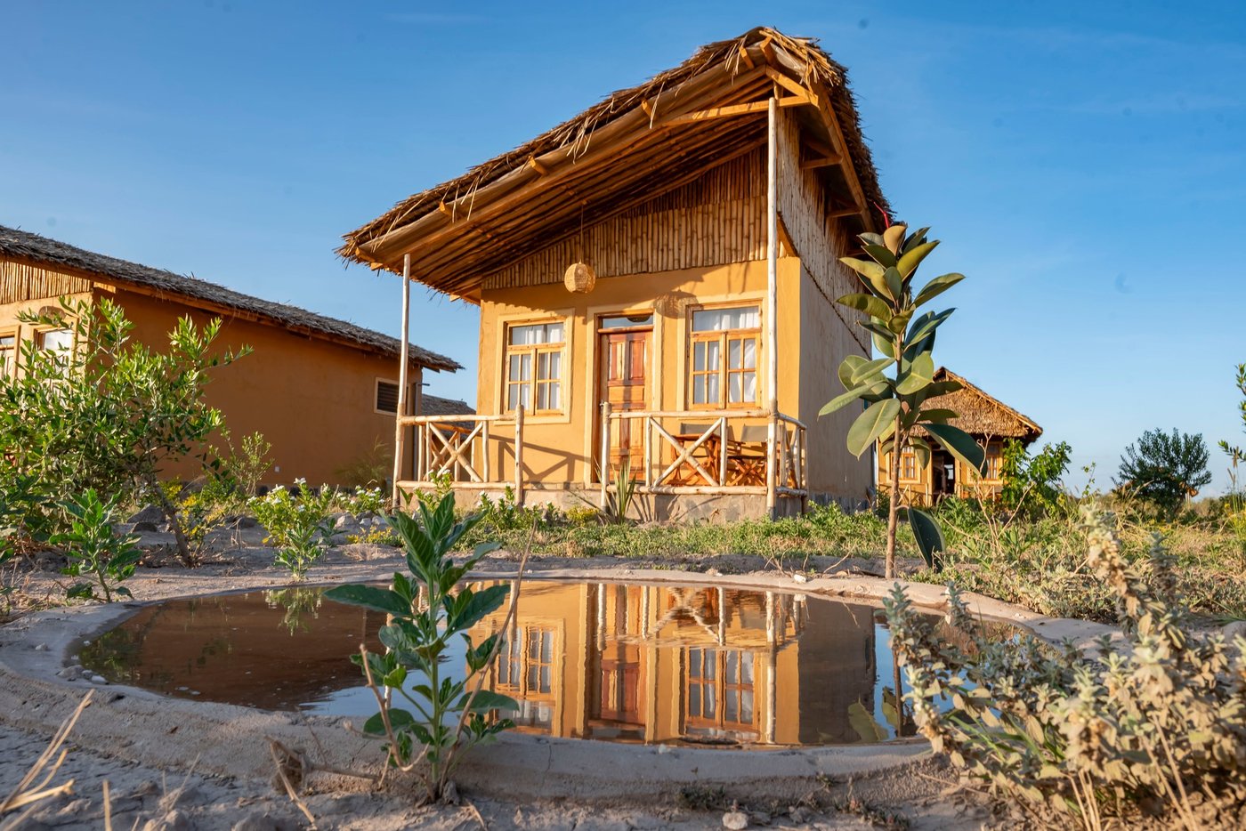 Thatched cottage with a veranda reflected in a garden pond at Amboseli Wildebeest Camp.
