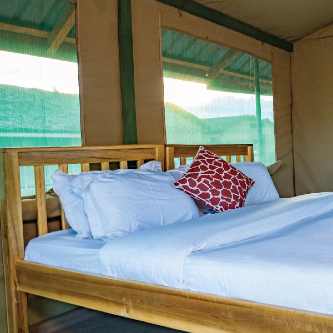 Bed with crisp white linen and a red accent pillow in a cottage at Amboseli Wildebeest Camp.