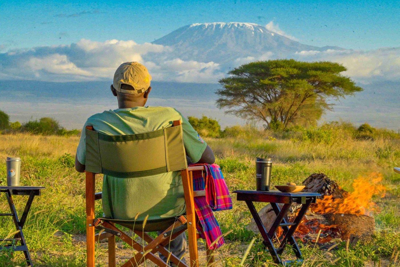 Guest relaxing by a campfire with Kilimanjaro on the horizon at Amboseli Wildebeest Camp.