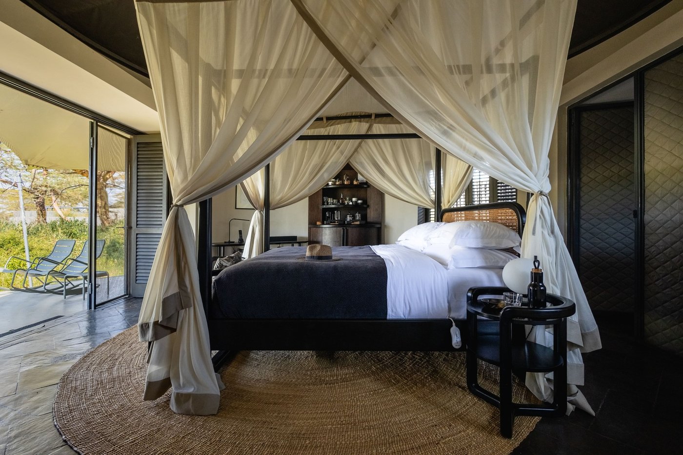 Four-poster bed draped in white linen opening onto the plains at Angama Amboseli.
