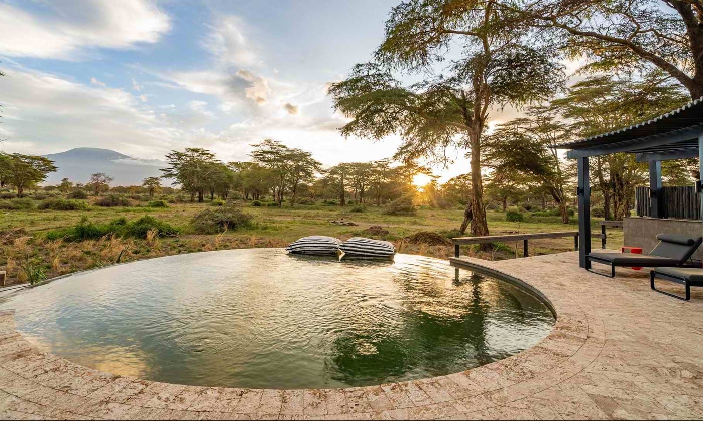 Circular infinity pool with loungers catching the sunrise at Angama Amboseli.