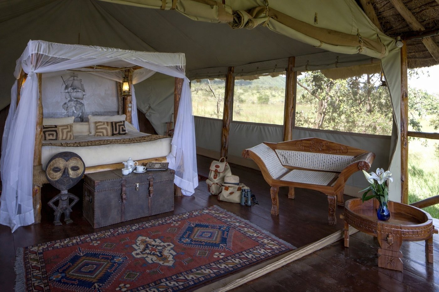 Canopied bed with tribal artwork and a woven rug in a tent at Campi ya Kanzi.