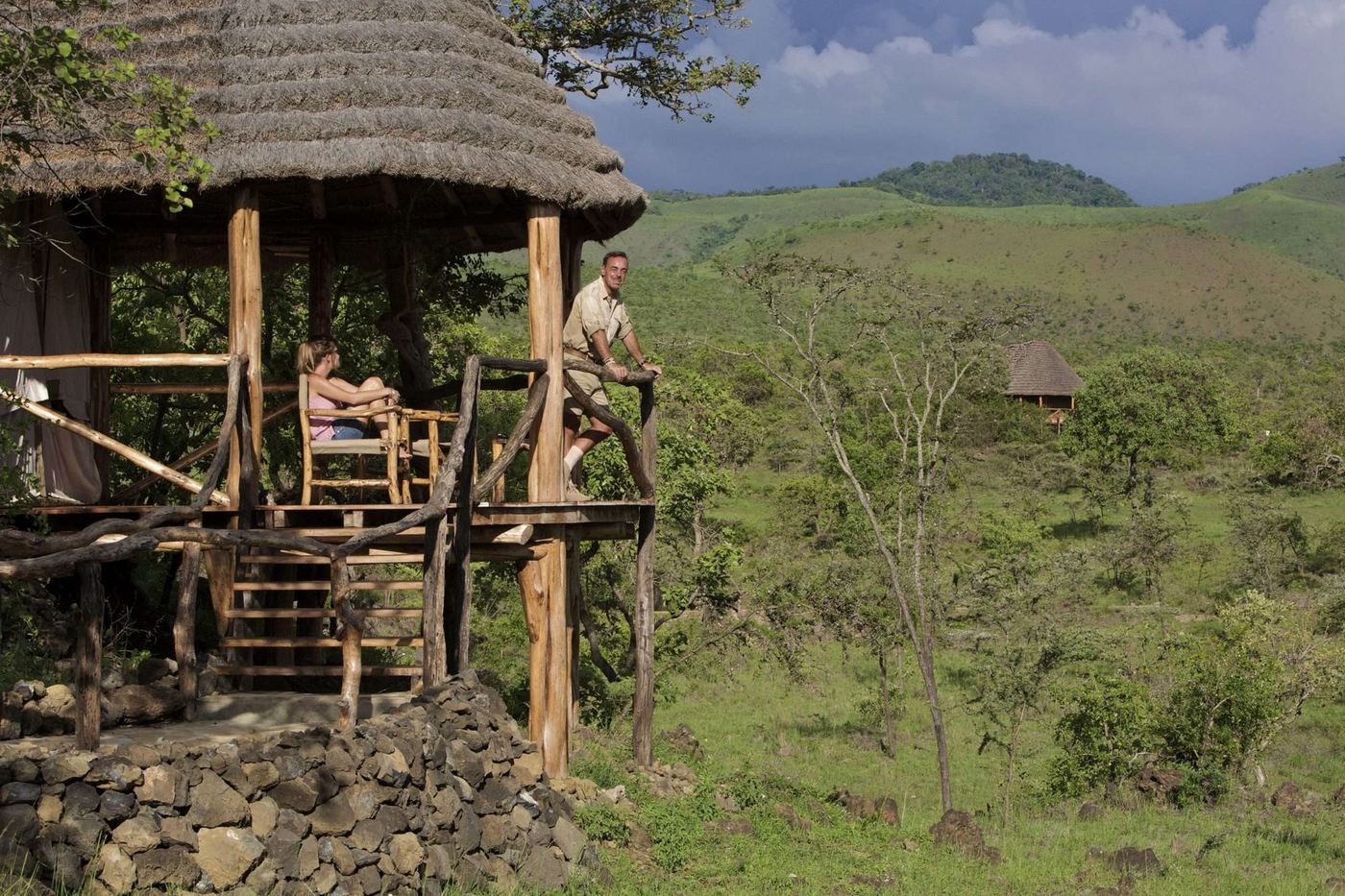 Guest resting on an elevated viewing platform overlooking green hills at Campi ya Kanzi.