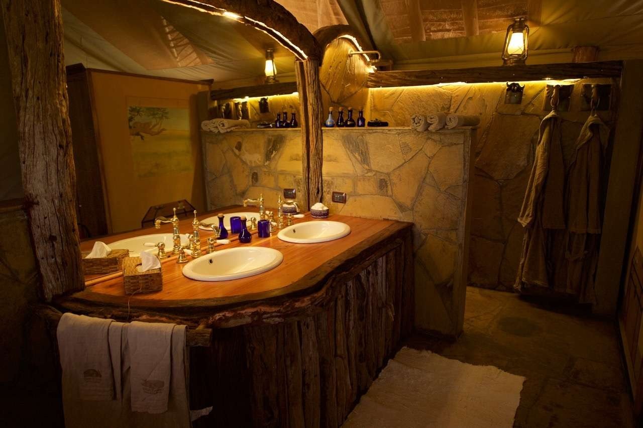 Double stone washbasins lit by warm lighting in a bathroom at Campi ya Kanzi.