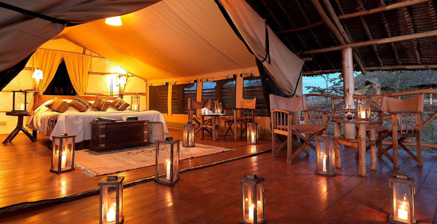Candlelit tent interior with a four-poster bed and dining table at Elerai Camp.