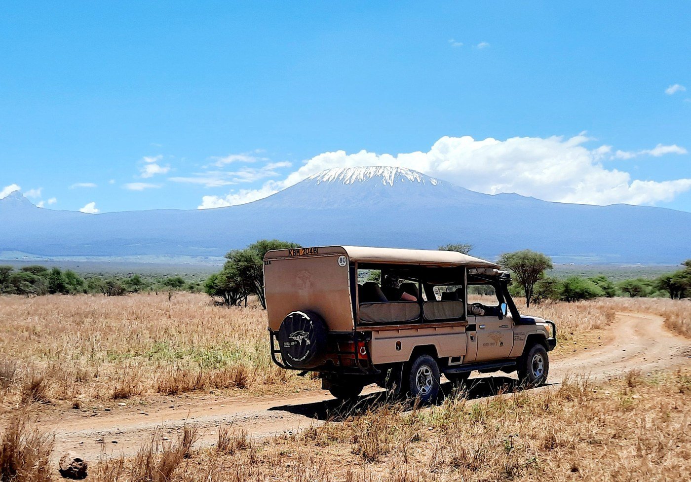 Safari vehicle driving a dirt track beneath Kilimanjaro near Elerai Camp.