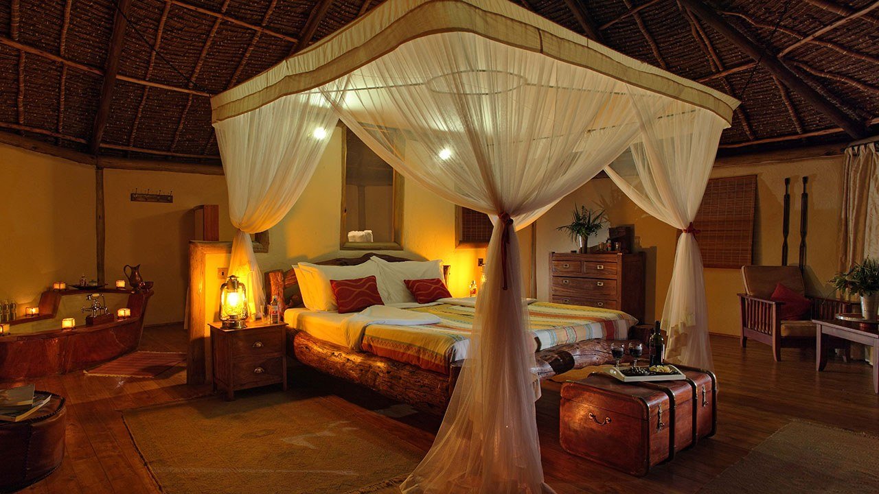 Canopied bed with mosquito netting in a thatched tent at Elewana Tortilis Camp.