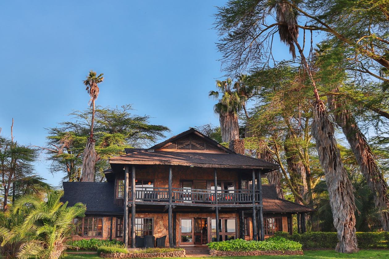 Two-storey wooden villa framed by palm trees on the lawns of Kibo Villa, Amboseli.