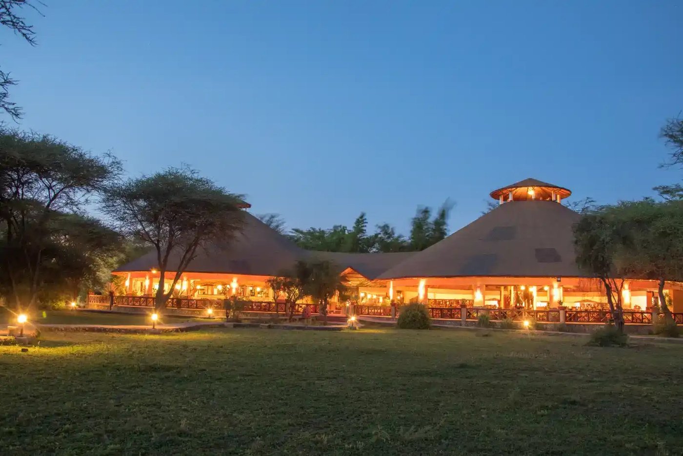 Round thatched lodge building glowing with warm lights at dusk at Kilima Safari Camp, Amboseli.