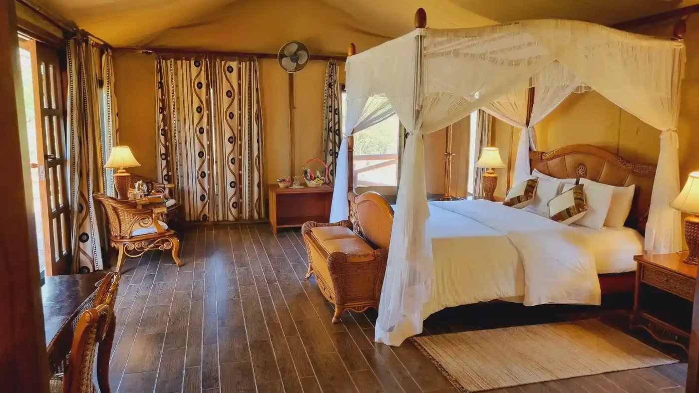 Carved wooden bed with a canopy frame and wood floors at Kilima Safari Camp.