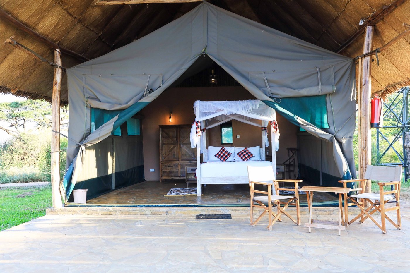 Open-fronted safari tent with a canopy bed and deck chairs at Oilepo Amboseli.