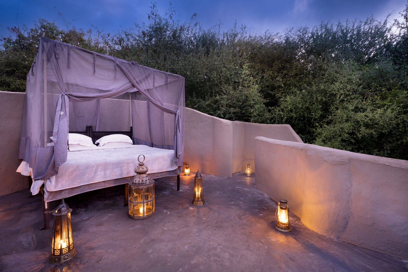 Outdoor four-poster bed on a stone terrace lit by lanterns at dusk at ol Donyo Lodge.
