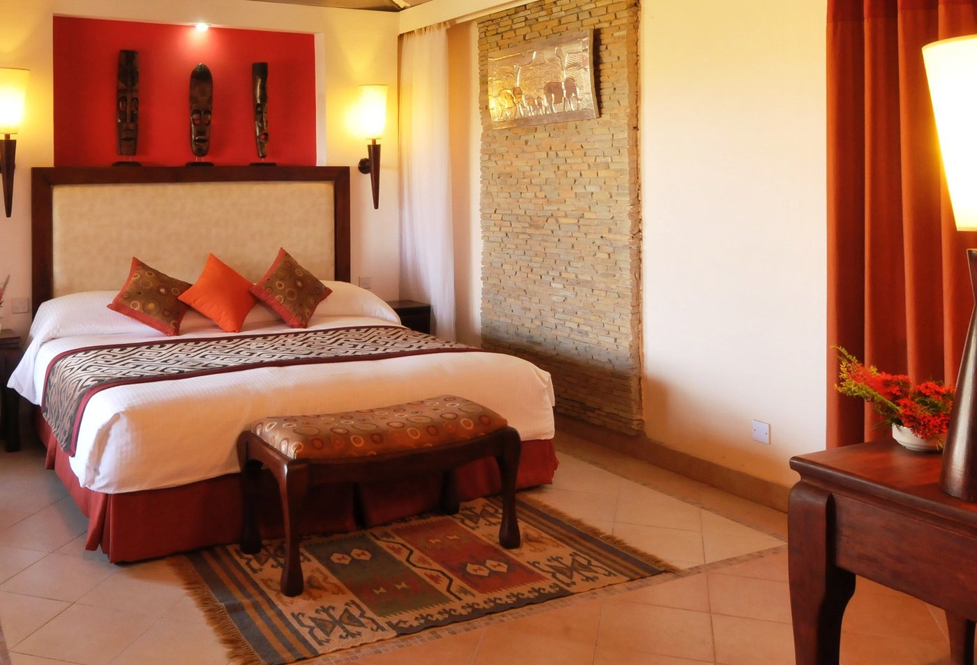 Bedroom with a carved wooden headboard and African wall masks at Ol Tukai Lodge.
