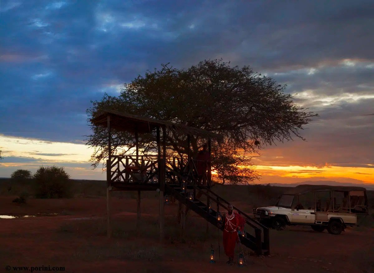 Elevated wooden viewing hide silhouetted against an orange sunset sky at Porini Amboseli Camp.