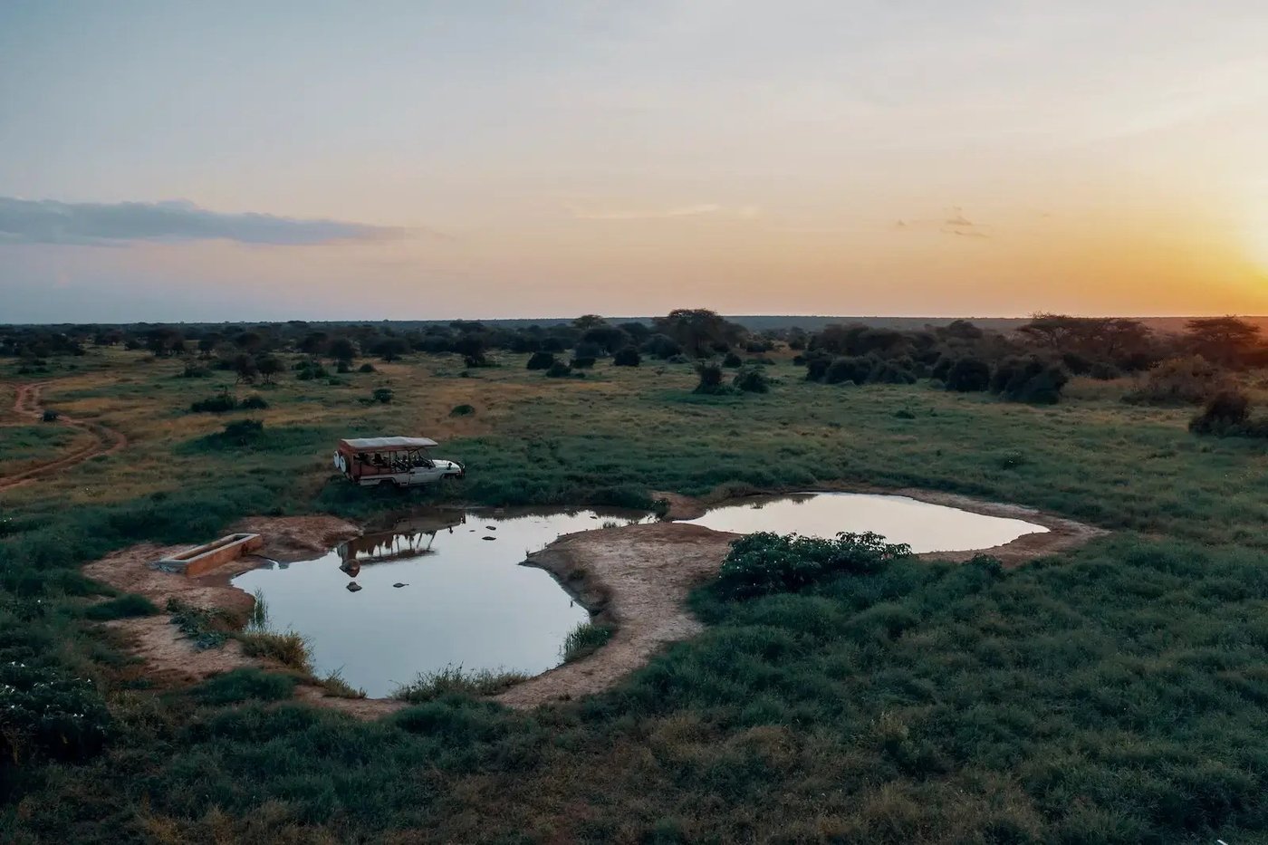 Aerial view of a waterhole with a vehicle parked beside it near Porini Amboseli Camp.