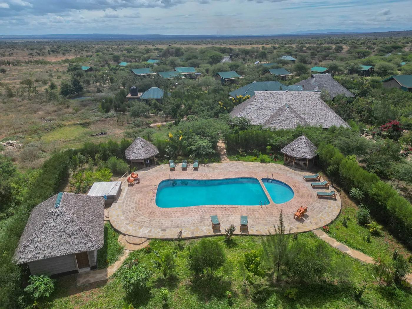 Aerial view of the thatched lodge and pool among green grounds at Sungura Safari Camp, Amboseli.