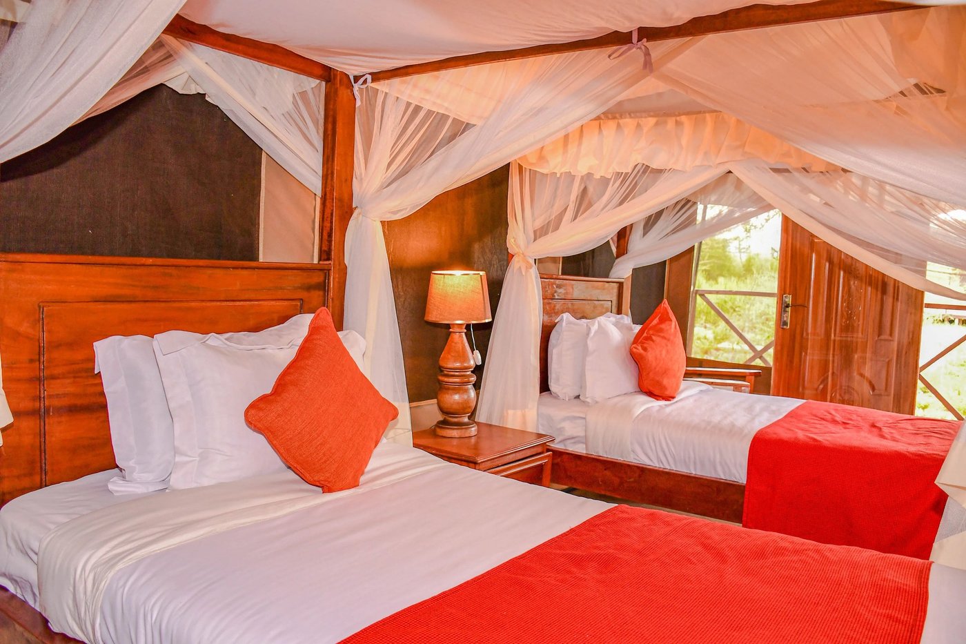 Twin beds draped in white mosquito netting with orange accents at Sungura Safari Camp.