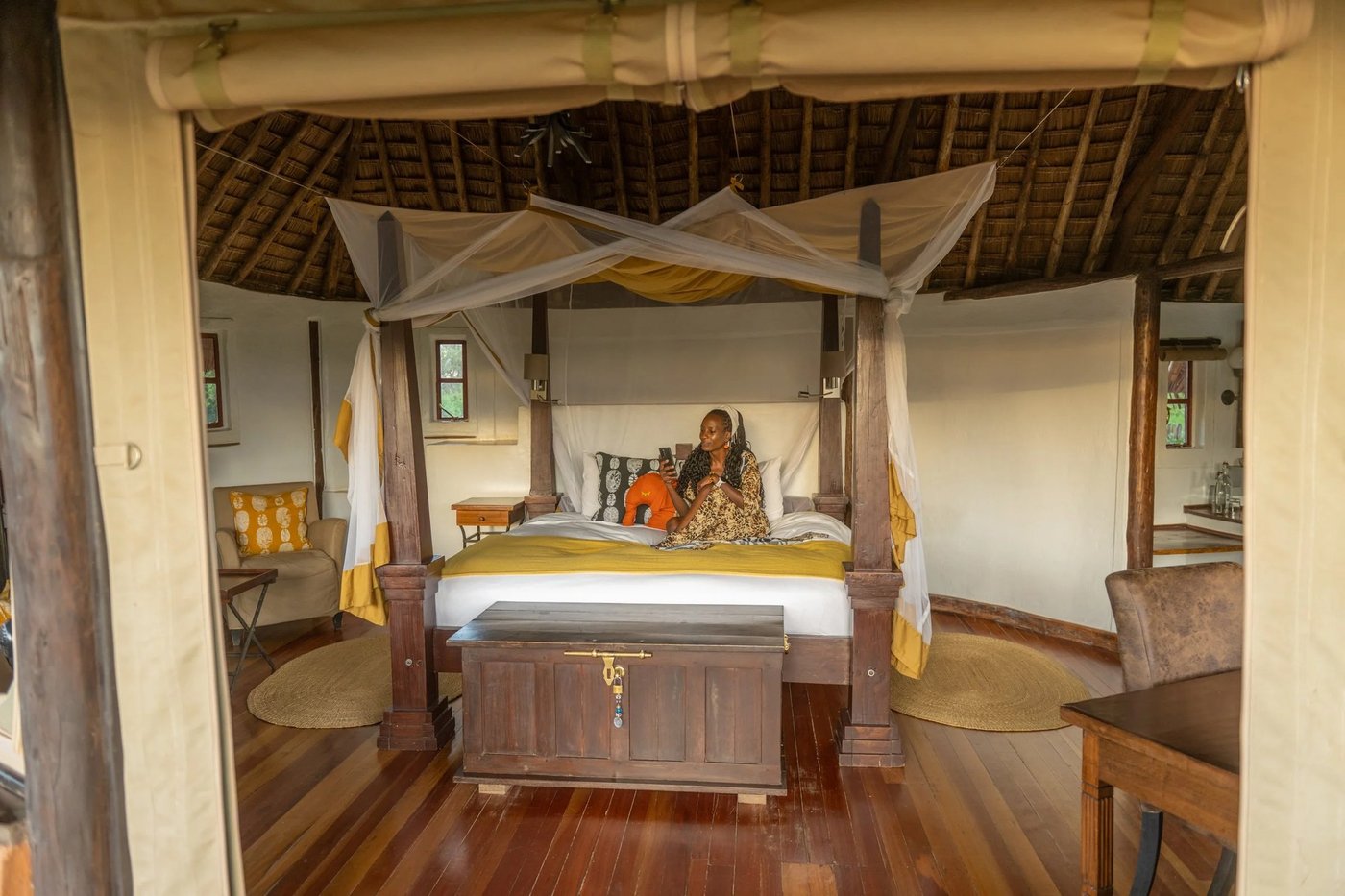 Guest relaxing on a four-poster bed under a thatched roof at Tawi Lodge.