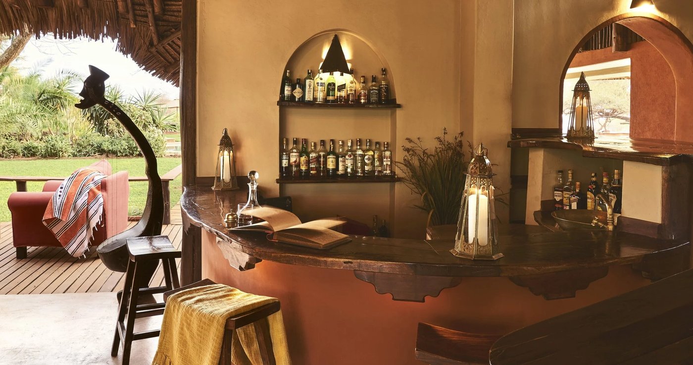 Warmly lit bar area with stocked shelves and leather stools at Tawi Lodge.